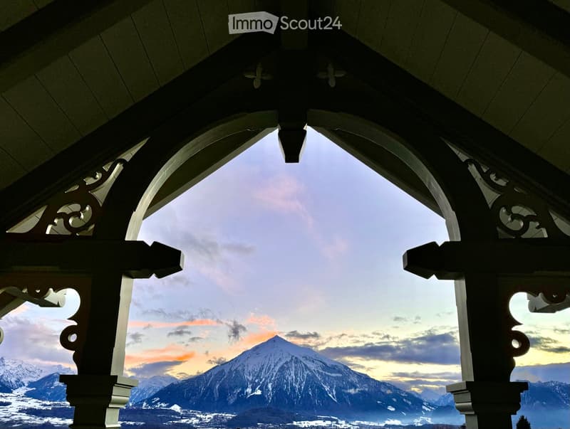 Balcony with ornate wooden railings, overlooking a snow-capped mountain range during sunset.
