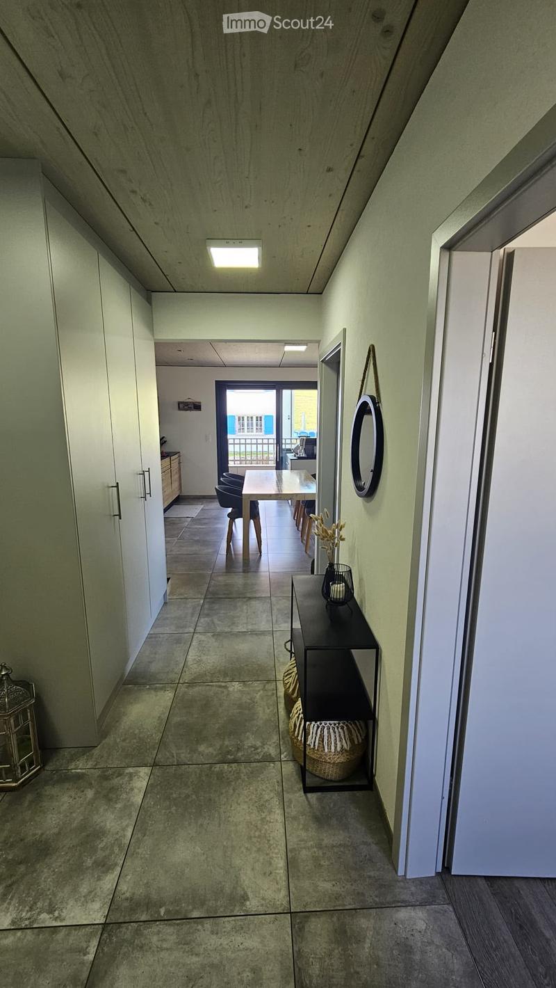Modern hallway with tiled flooring, white walls, and built-in storage cabinets. Features a small black console table with a decorative vase and a round mirror on the wall.
