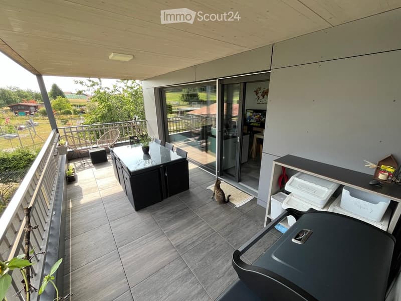 Balcony with tiled floor, glass sliding doors, outdoor furniture including a table, chairs, and a cat sitting on the floor.