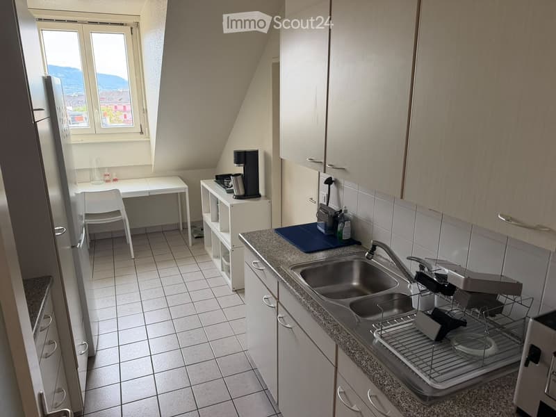 Modern kitchen with white cabinets, granite countertop, double sink, and a small desk area with a chair.