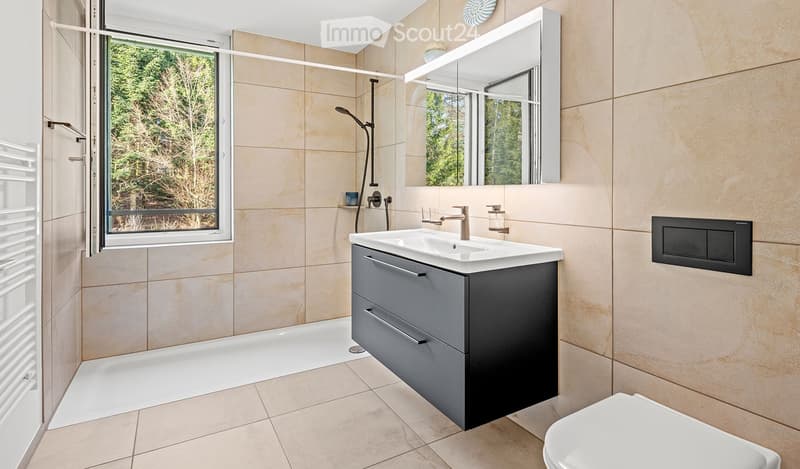 Modern bathroom with beige tiles, a large mirror, a sink with a modern faucet, a shower area, and a toilet.