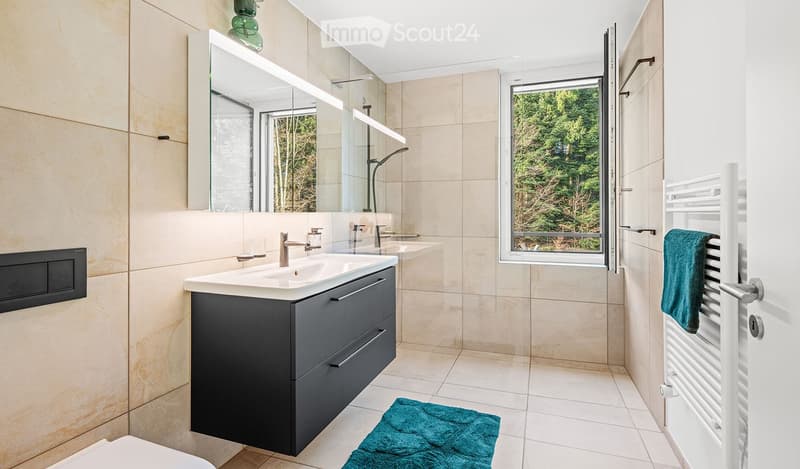 Modern bathroom with a double sink vanity, large mirror, radiator, and a view of greenery through a window.