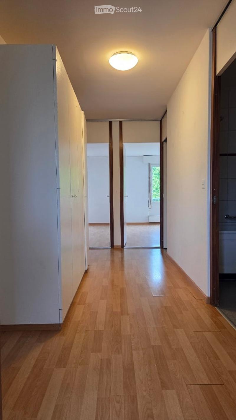 Empty hallway with wooden flooring, white walls, and a ceiling light fixture. Doors lead to adjacent rooms.