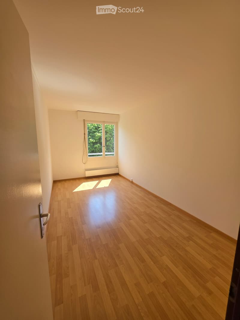 Empty room with light wooden flooring, white walls, and a window letting in natural light.