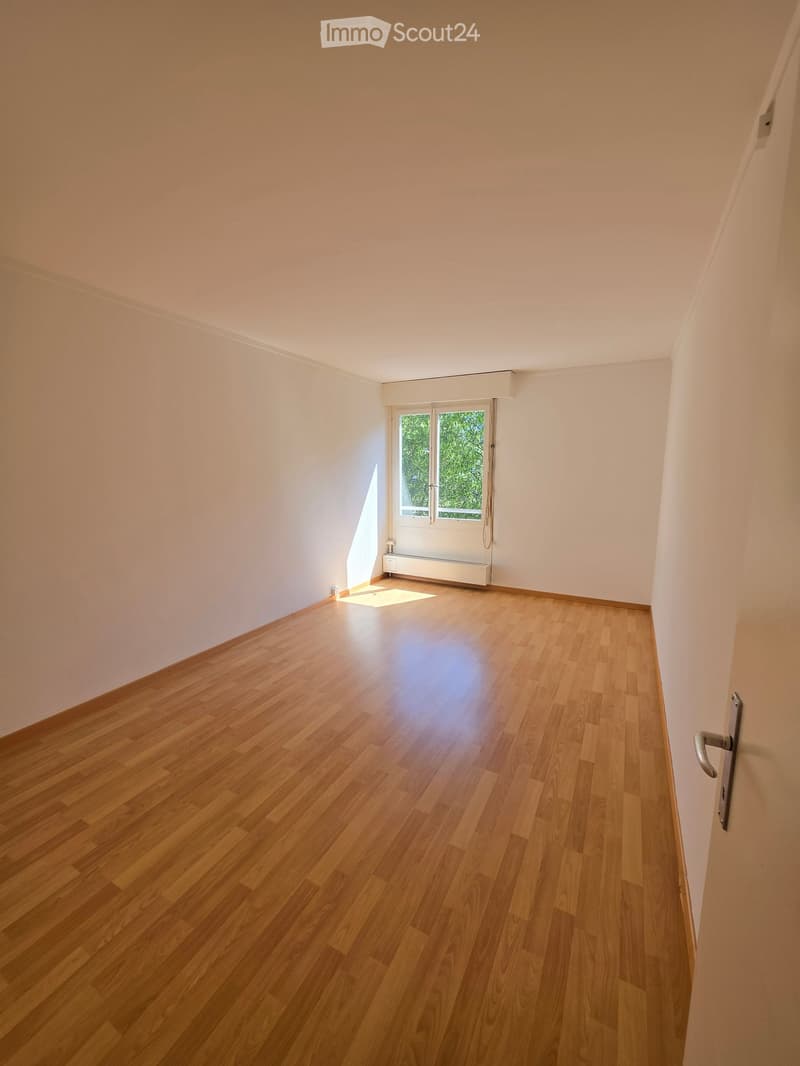Empty room with wooden flooring, white walls, and a window with a view of greenery. No furniture or equipment is present.