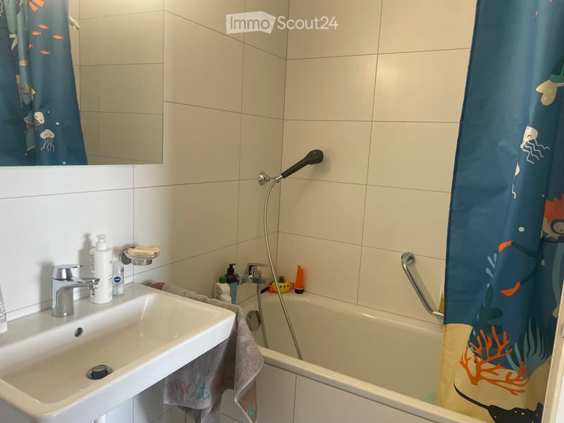 Bathroom with a white sink, bathtub, shower curtain, and various toiletries on the sink counter.