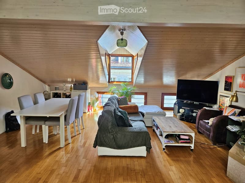 Bright, open living space with wooden floors, a large skylight, and modern furnishings including a sofa, coffee table, dining table, and TV.