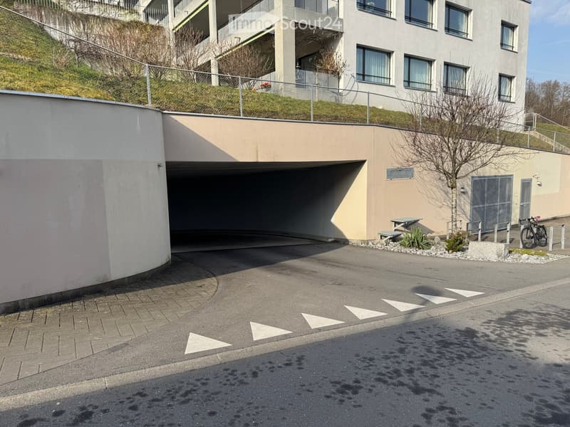Modern multi-story building with a garage entrance, small garden area, and a bicycle parked nearby.