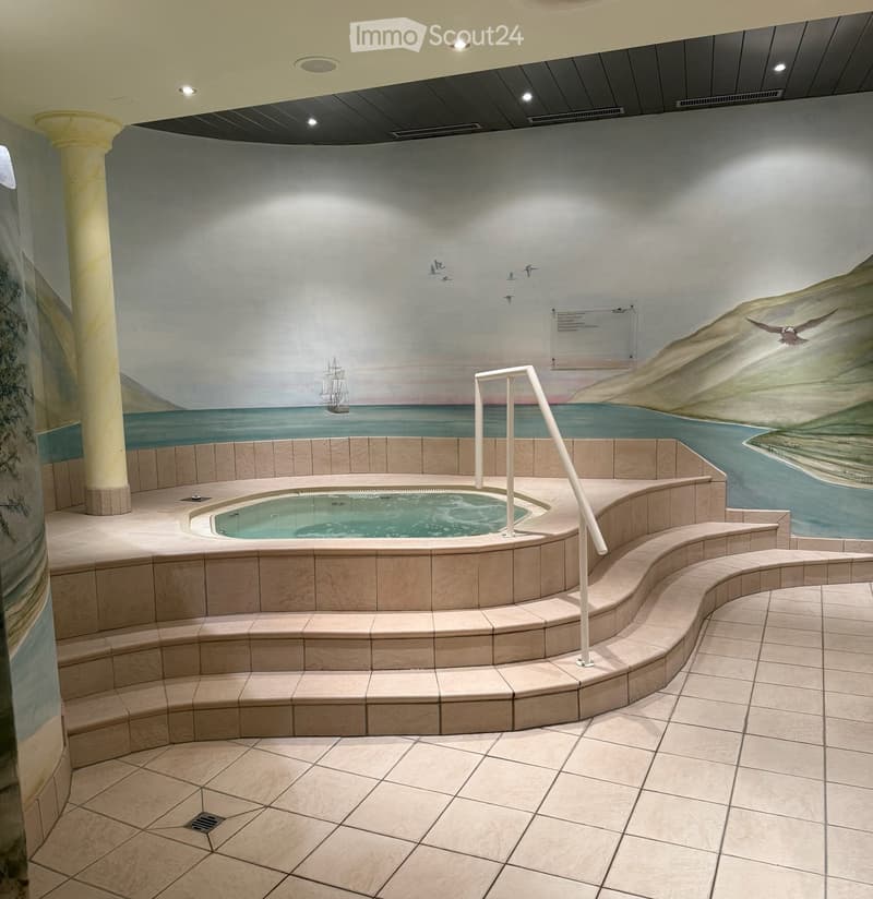 Spa-like bathroom with a large bathtub surrounded by tiled steps and a handrail, featuring a mural of a coastal scene with a ship and birds.