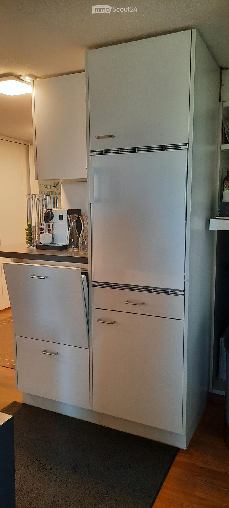 Modern kitchen with white cabinets, a refrigerator, coffee maker, and decorative vases on the counter.