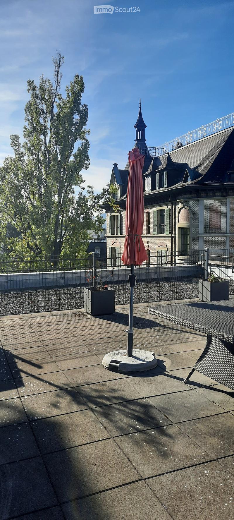 Roof terrace with concrete floor, metal railing, umbrella stand, and potted plants.