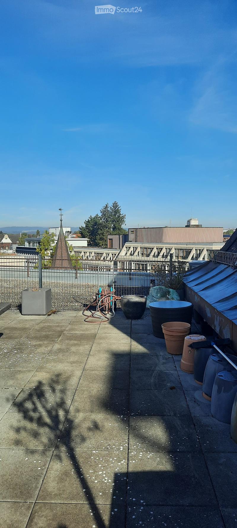 Rooftop patio with concrete floor, metal fence, and various containers including pots and barrels.