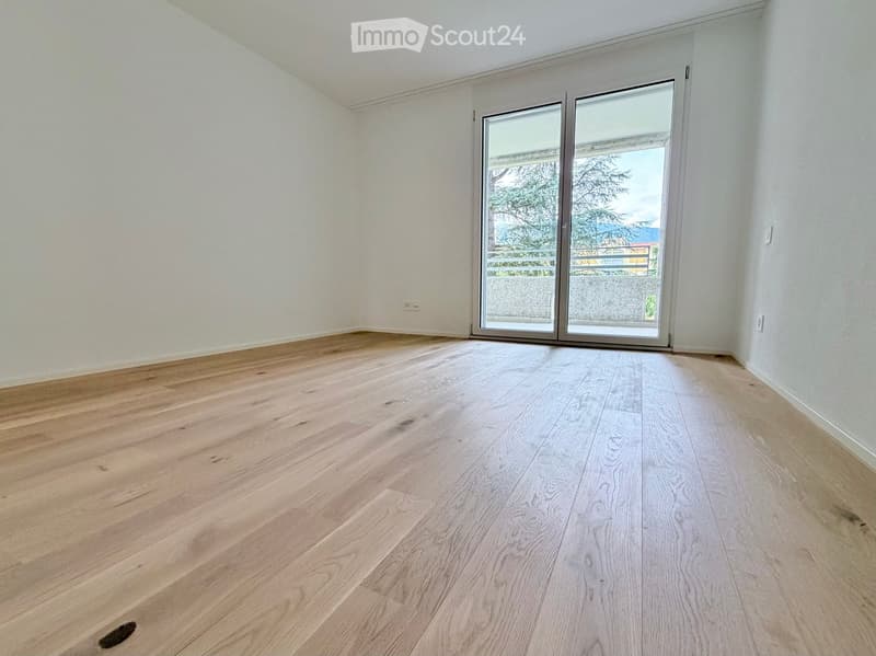 Empty room with light wooden flooring and white walls, featuring large sliding glass doors that open to a balcony or outdoor area.