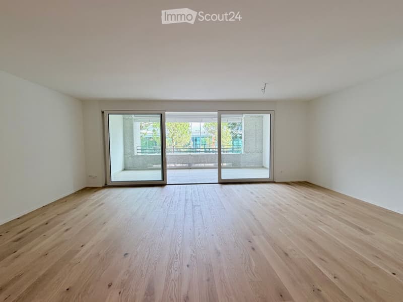 Empty room with light wooden flooring and large sliding glass doors leading to a balcony area.