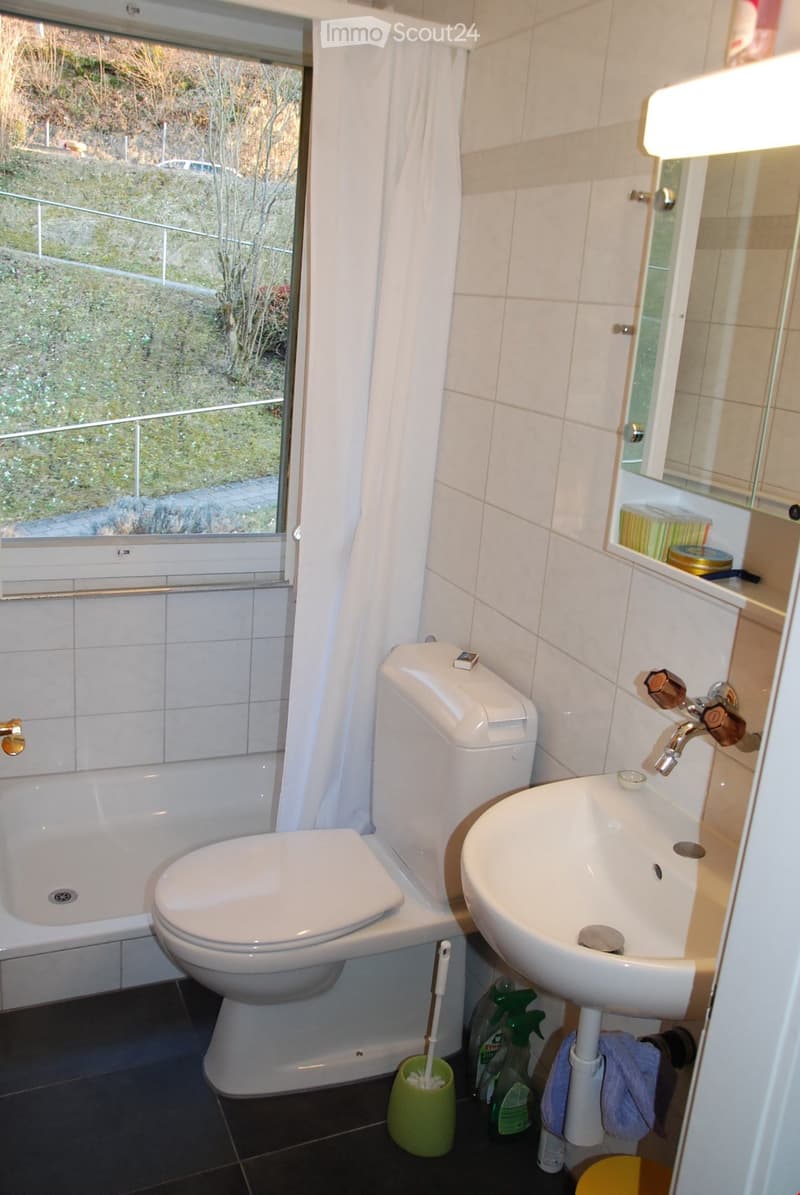 Bathroom with a bathtub, toilet, and sink. White tiles and fixtures. A window with a view.