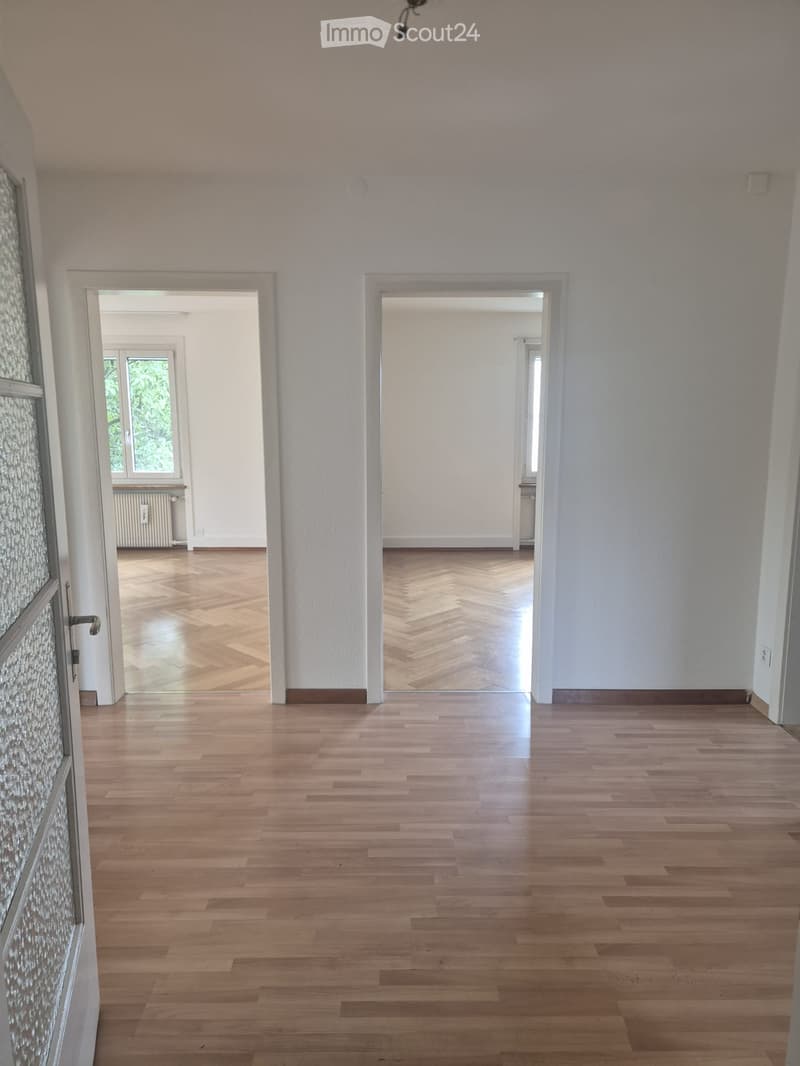 Empty hallway with light wooden flooring, white walls, and two open doorways leading to other rooms.