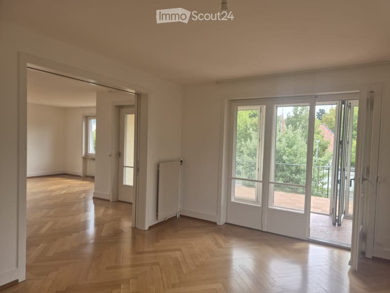 Empty room with wooden flooring, white walls, large sliding glass doors leading to a balcony, and visible radiators.