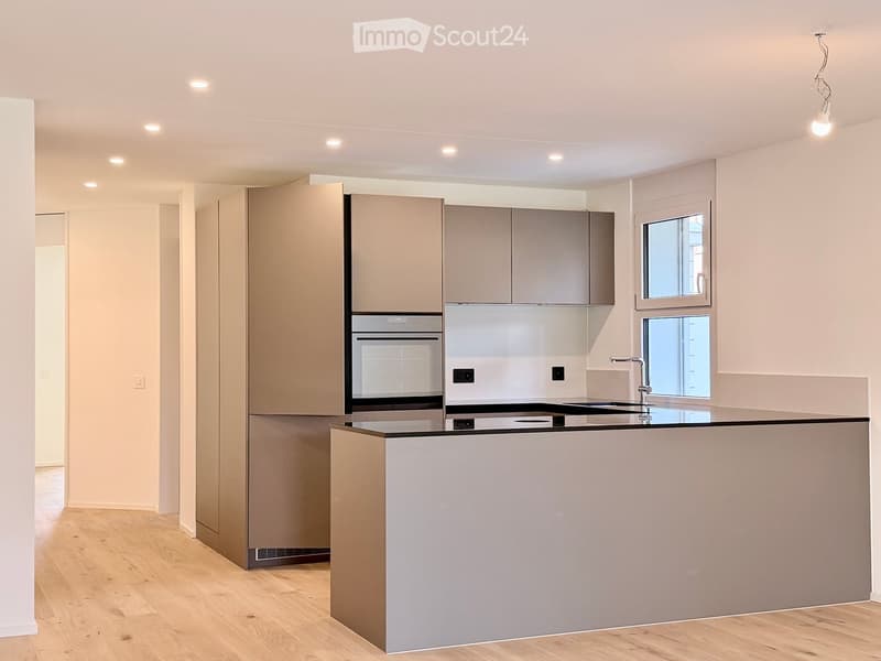 Modern kitchen with light grey cabinets, a central island, and built-in appliances including an oven and sink.