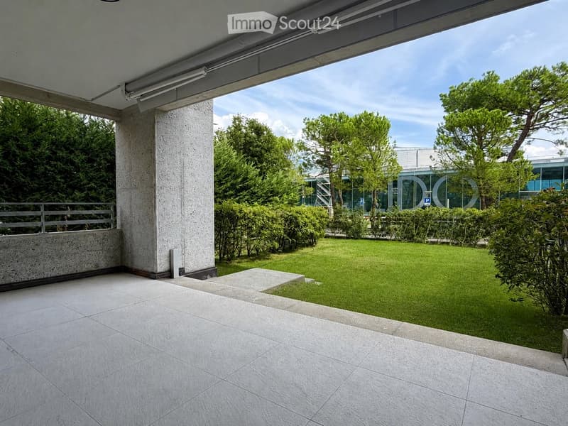 Balcony with tiled floor, concrete column, metal railing, and view of a well-maintained lawn and trees.