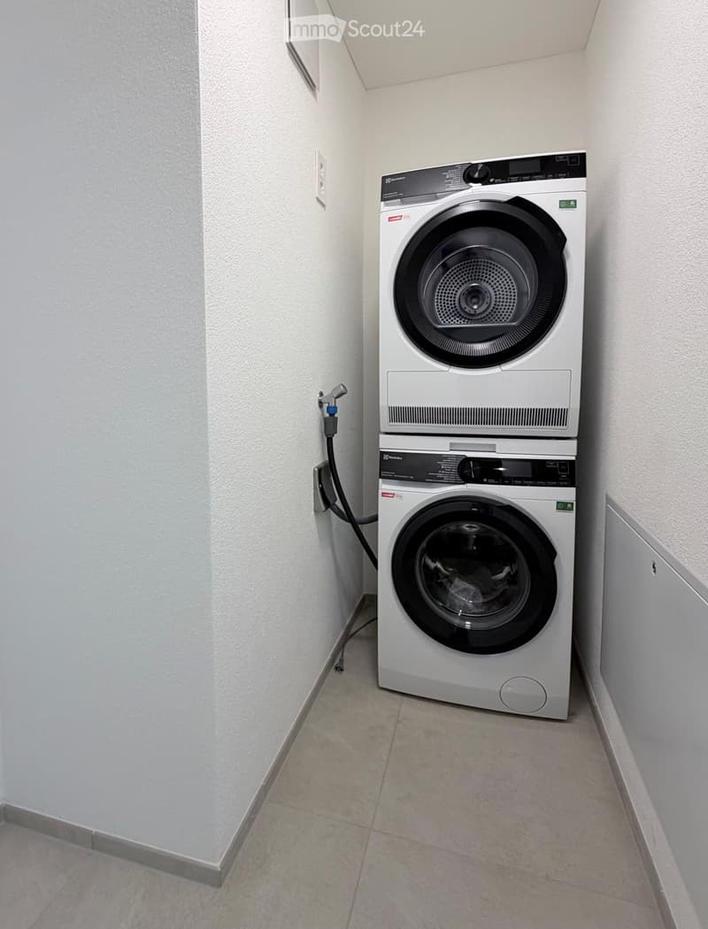 A compact bathroom with a stacked washing machine and dryer unit, tiled floor, and white walls.