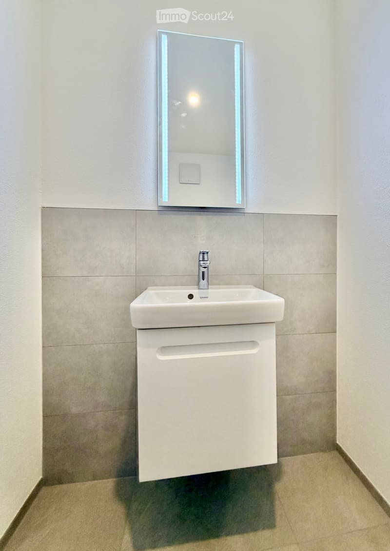 Modern bathroom with a white sink, sleek mirror with LED lighting, and a built-in cabinet below.