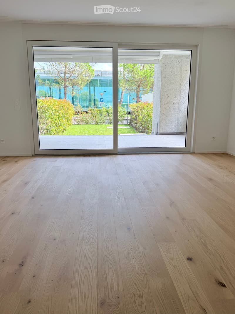 Empty room with light wooden flooring and large sliding glass doors leading to a balcony or outdoor area. The walls are painted a light neutral color, and the space is well-lit with natural light.