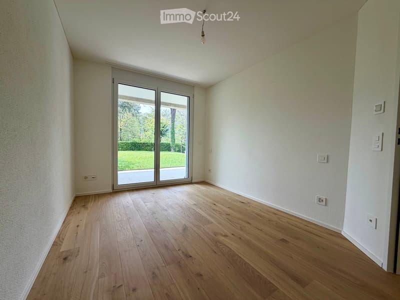 Empty room with light wooden flooring, white walls, and a large sliding glass door leading to a green outdoor area.