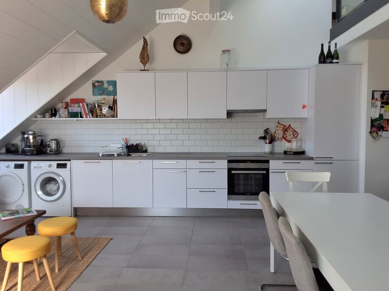Modern kitchen with white cabinets, stainless steel appliances, and a breakfast area with yellow stools and a white table.