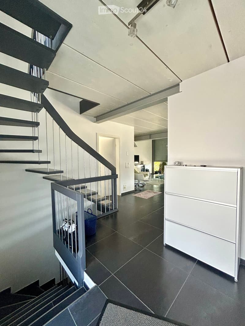 Modern hallway with dark tiled floor, staircase with metal railing, white walls, and a small blue basket on the stairs. A white cabinet is visible on the right side.