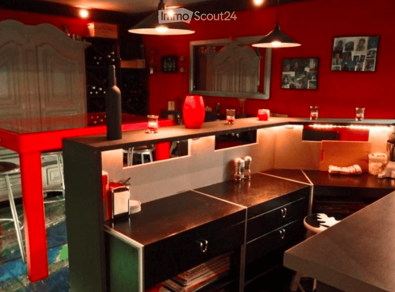 Modern kitchen with red walls, black countertops, bar counter, stools, wine bottle, candles, mirror, framed pictures, salt and pepper shakers, and a wine rack.
