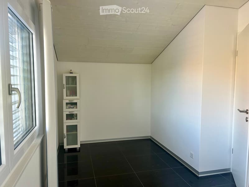 A small, unfurnished room with white walls, black tiled floor, and a single cabinet with glass doors and drawers.
