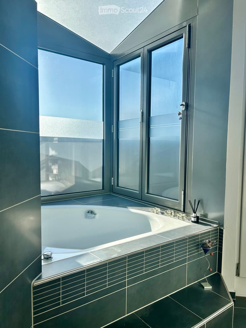 Modern bathroom with a large bathtub, sleek sink, and large windows offering a view of the adjacent room.