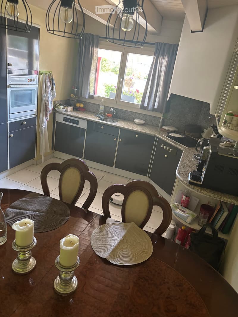 Modern kitchen with dark blue cabinets, stainless steel appliances, granite countertops, and a dining area with a wooden table and chairs.