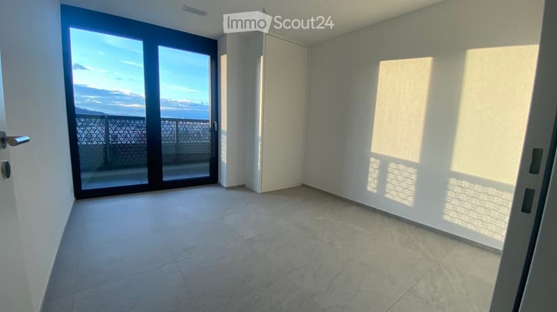 Empty room with tiled floor, large sliding glass door leading to a balcony with a view, and white walls.