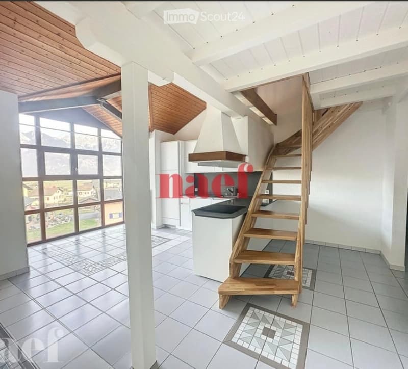 Bright kitchen with large windows offering a scenic view, featuring a wooden staircase leading upwards, a sink, a refrigerator, and a range hood.