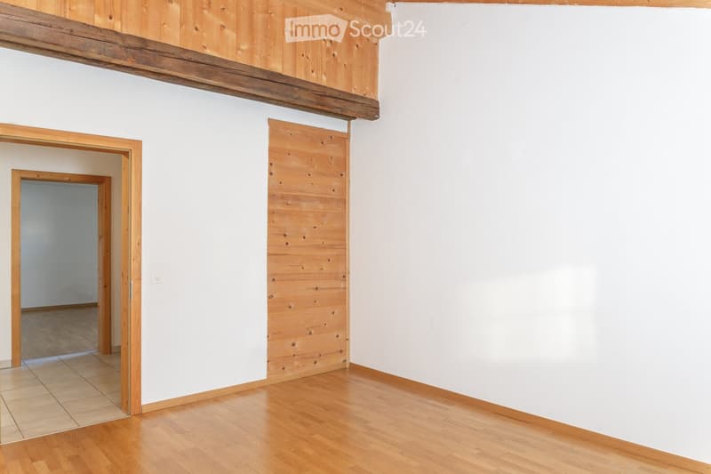 Empty room with wooden flooring, white walls, and wooden paneling on one wall. There are two doorways leading to other spaces.