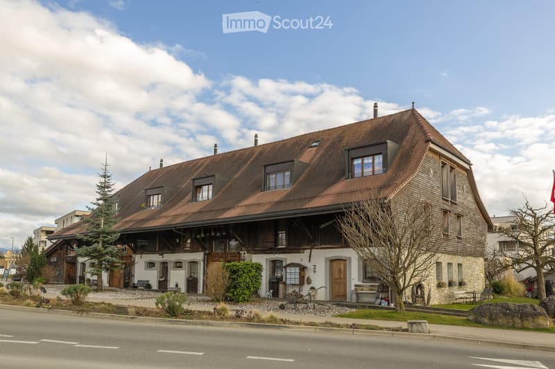 Two-story traditional house with a brown tiled roof, wooden facade, multiple windows, and a small garden area in front.