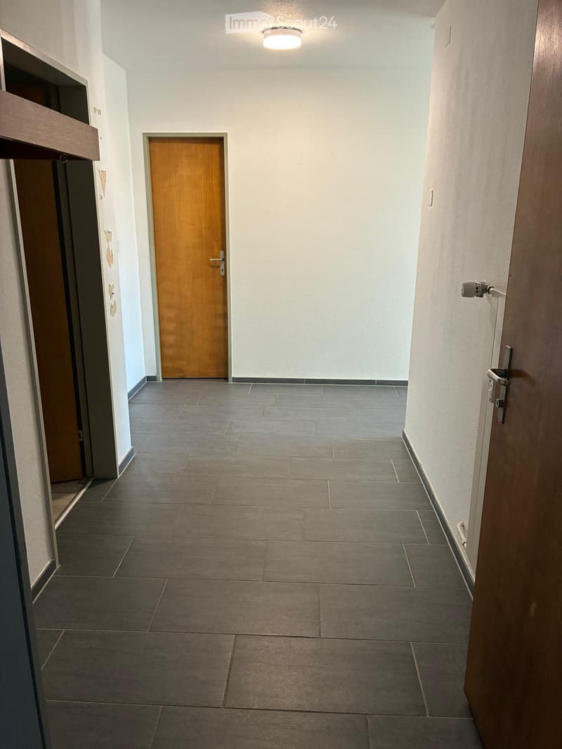 Empty hallway with tiled floor, white walls, and a single wooden door.