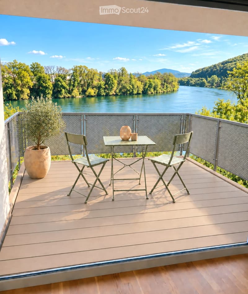 Balcony with wooden decking, metal railing, table with two chairs, vase, and cup, overlooking a river and green landscape.