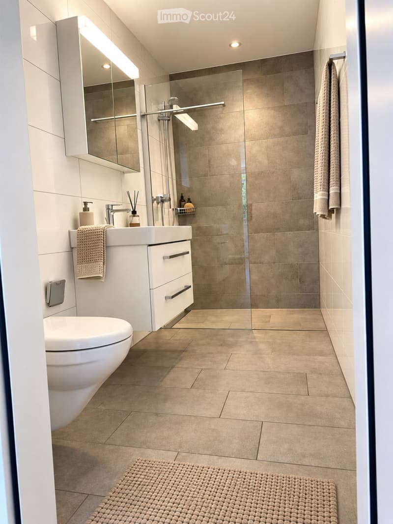 Modern bathroom with a white toilet, sink, and mirrored cabinet. Features a glass-enclosed shower with a modern faucet and towel racks.