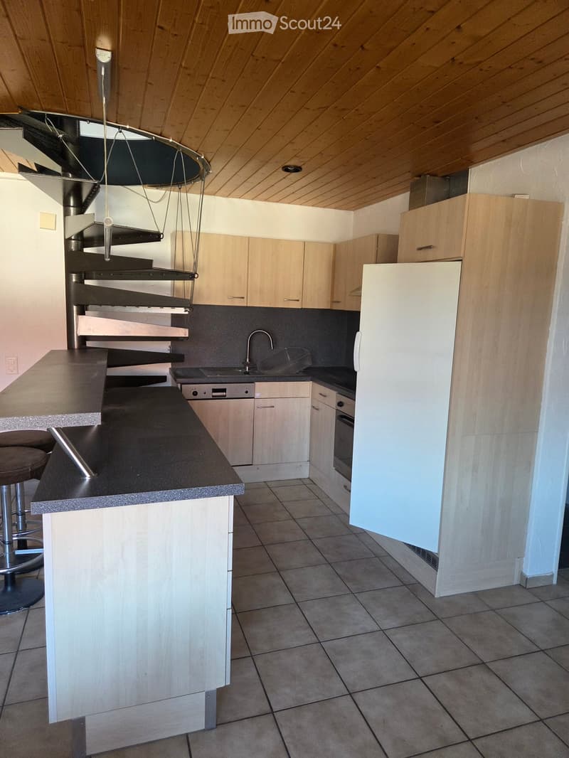 Modern kitchen with light wood cabinets, black countertops, stainless steel appliances, and a central island with bar stools.
