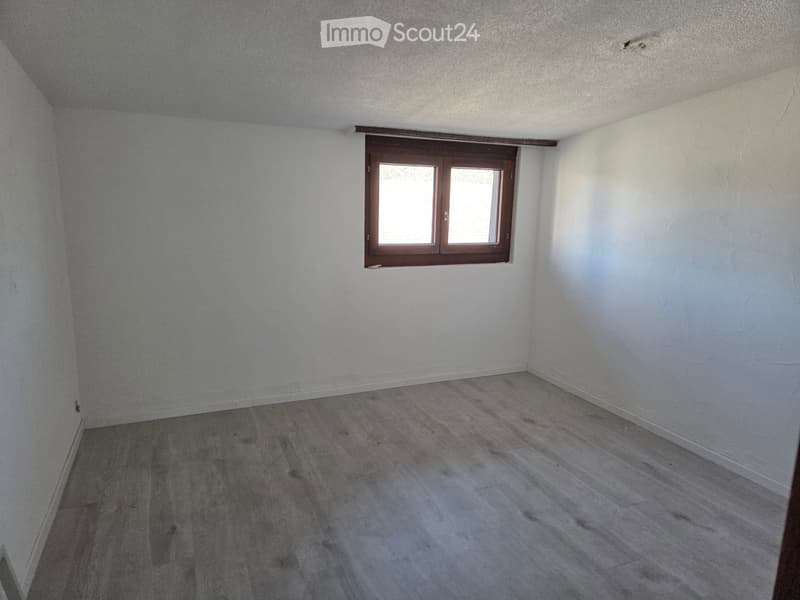 Empty room with light-colored walls and wooden flooring, featuring a single window with wooden frame.
