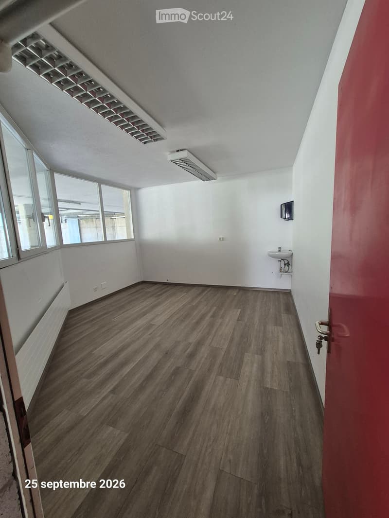 Empty room with wooden flooring, white walls, and a small sink in the corner. Large windows provide natural light, and the ceiling has a modern ventilation system.