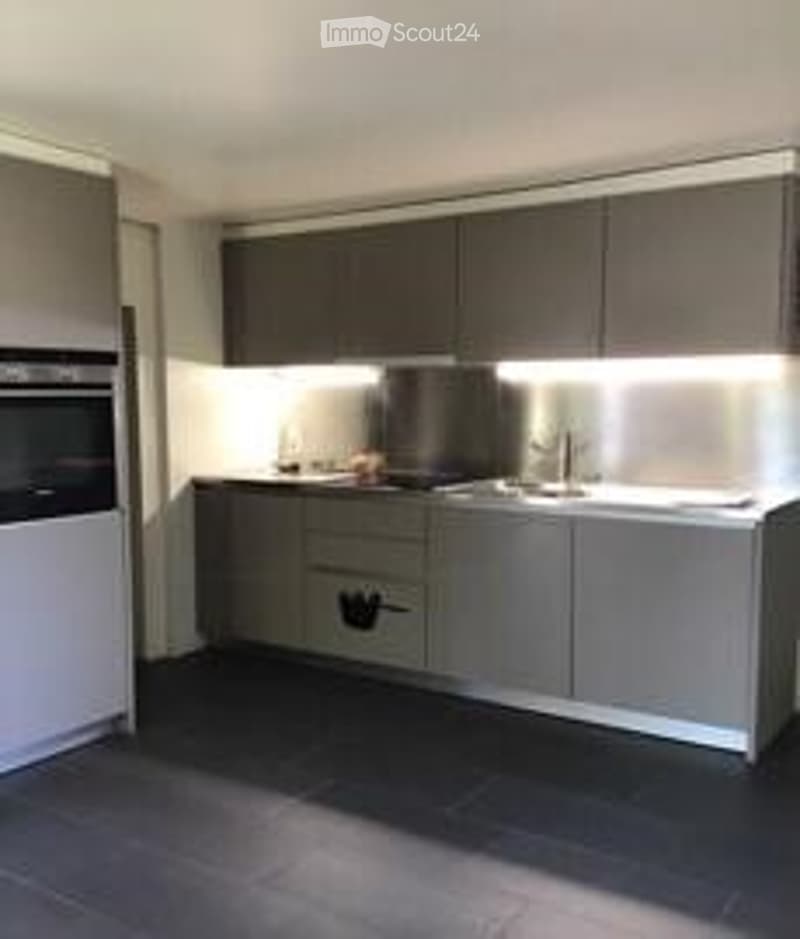 Modern kitchen with grey cabinets, a built-in oven, a sink with a faucet, and dark tiled flooring.