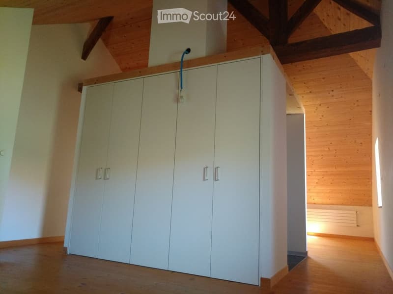 Empty room with wooden floor and white built-in wardrobes, exposed wooden beams on the ceiling.