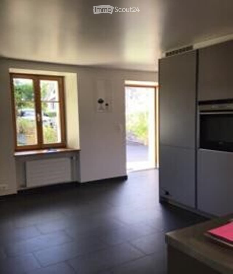 Empty room with tiled floor, white walls, large window with wooden frame, radiator, and grey cabinetry.