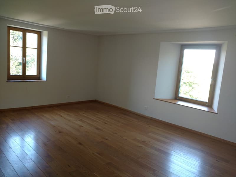 Empty room with wooden flooring, two windows, and white walls.
