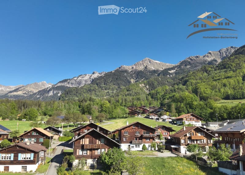 traditional alpine houses, surrounded by mountainous terrain, green landscape, brown facades, blue accents