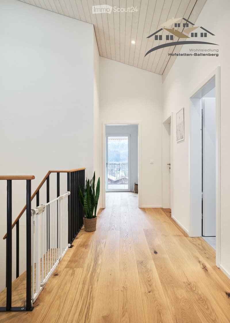 Hardwood floor, white walls, a potted plant on the staircase, white railing on the staircase, a picture frame on the wall, a balcony through a glass door