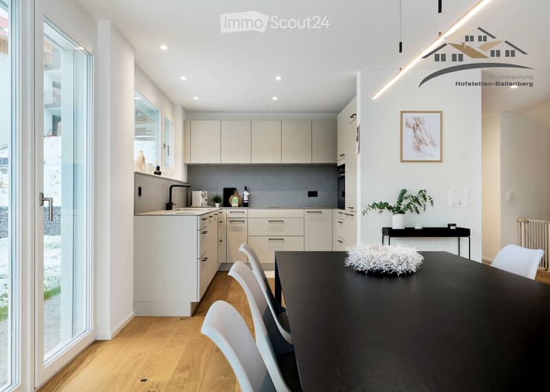 Modern kitchen with wooden floor, white cabinets, stainless steel sink, and sliding glass doors leading to an outdoor area.